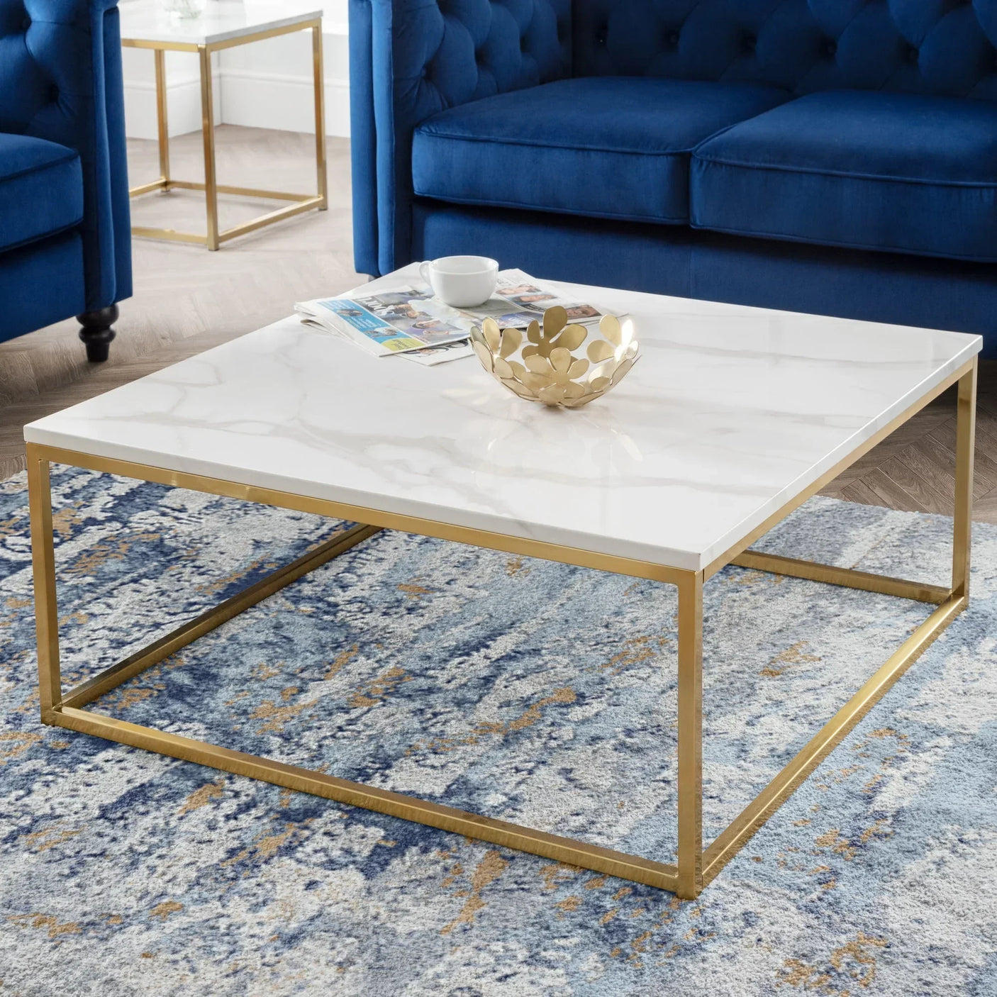 Gold coffee table with white marble top in living room with blue sofa and patterned rug