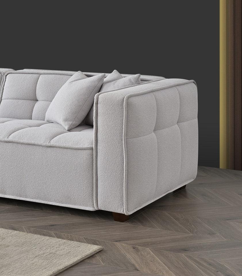 Light grey fabric sofa with tufted cushions and two pillows on wood herringbone floor