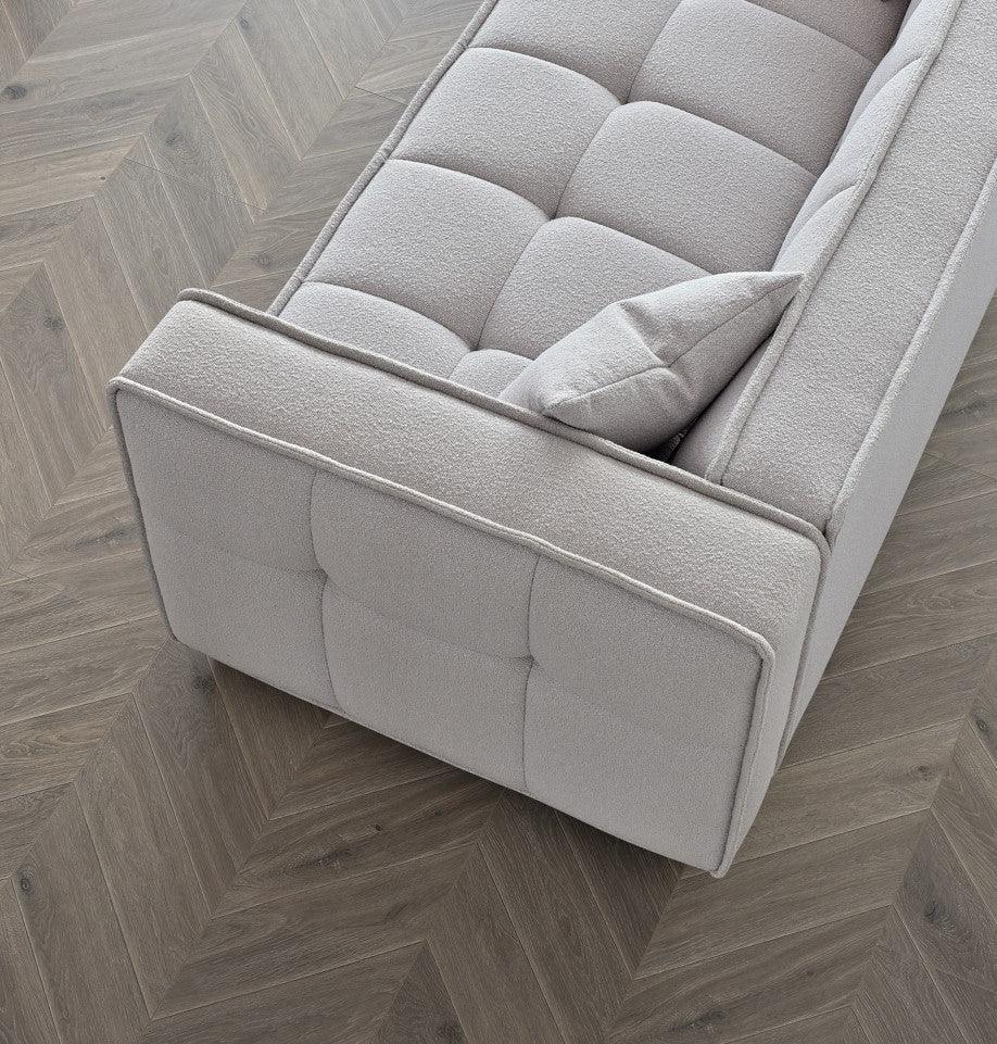 Light grey fabric sofa with tufted seat and side panel on herringbone wooden floor
