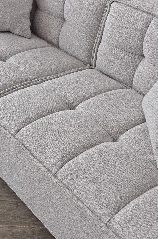Close-up of light grey fabric sofa with tufted cushions and textured upholstery