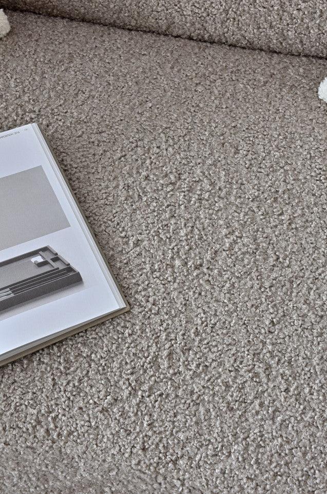 Beige boucle fabric sofa surface with book resting on seat cushion, close-up detail view