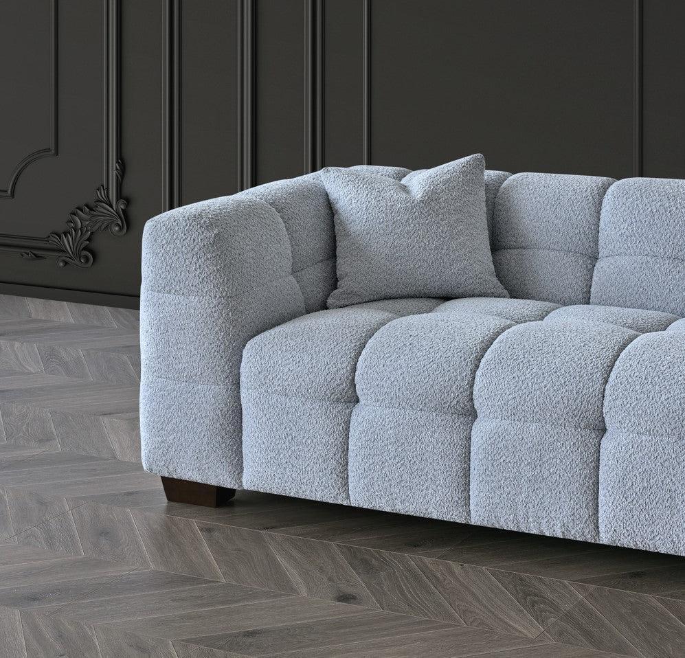 Light grey fabric sofa with tufted upholstery and matching cushion on herringbone wood floor