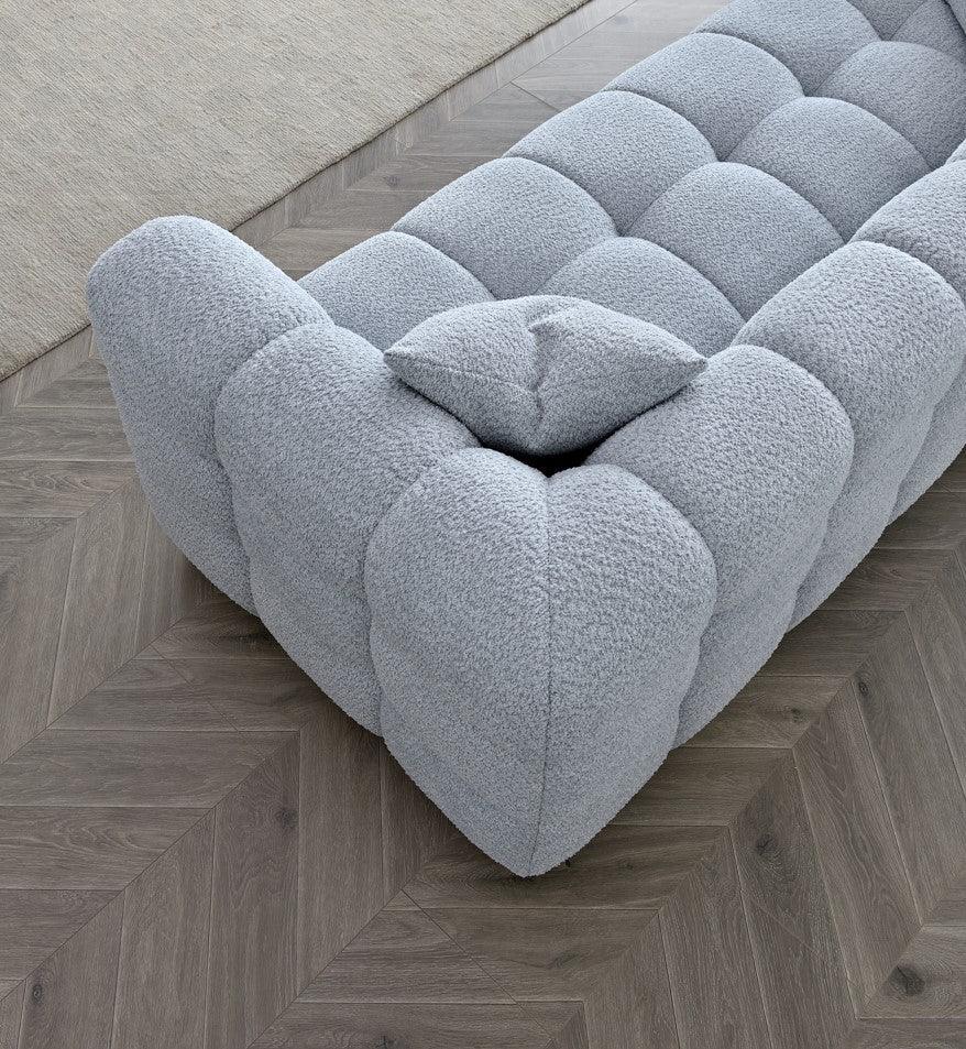 Light grey textured fabric sofa with deep tufting, set on herringbone wood flooring