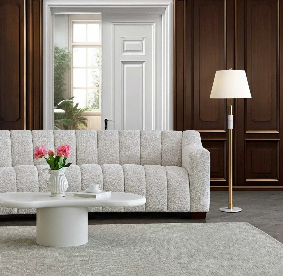 Modern cream sofa with textured upholstery, oval coffee table, and gold floor lamp in living room