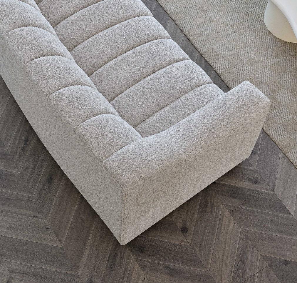 Curved beige fabric sofa with channel tufting on herringbone wood floor