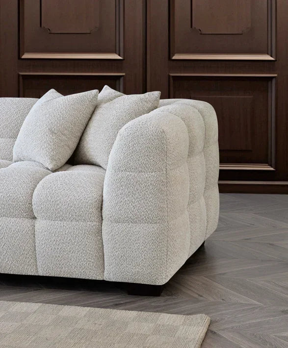 Beige textured fabric sofa with tufted design and scatter cushions near wooden wall panel