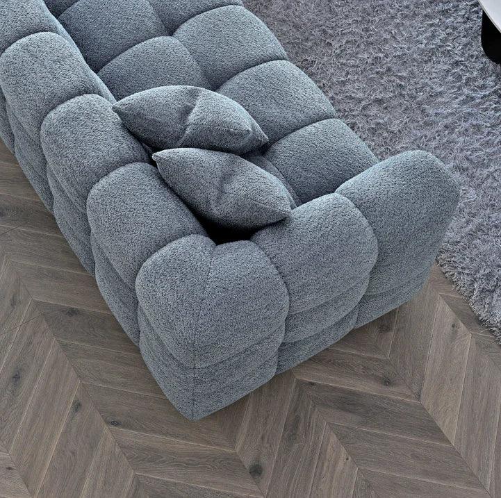 Grey textured fabric sofa with matching cushions on wooden herringbone floor near rug