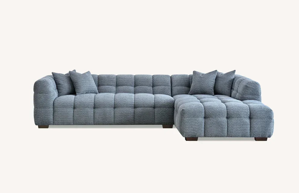 Grey corner sofa with quilted upholstery and scatter cushions on light background