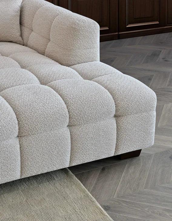 Cream boucle sofa corner with deep tufting on chevron wood floor and beige rug