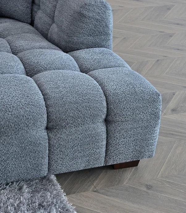 Close-up of tufted grey fabric sofa corner with wooden leg on herringbone floor