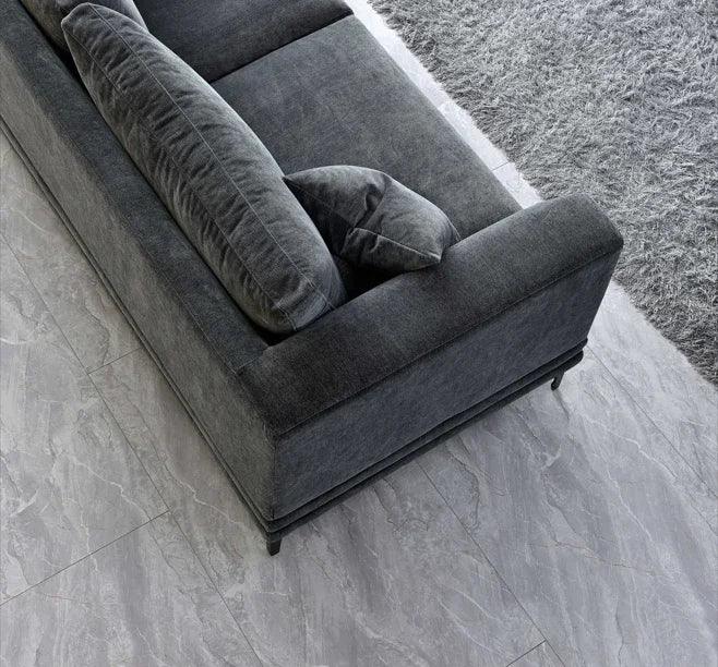 Dark grey fabric sofa with matching cushion on light marble floor and grey rug
