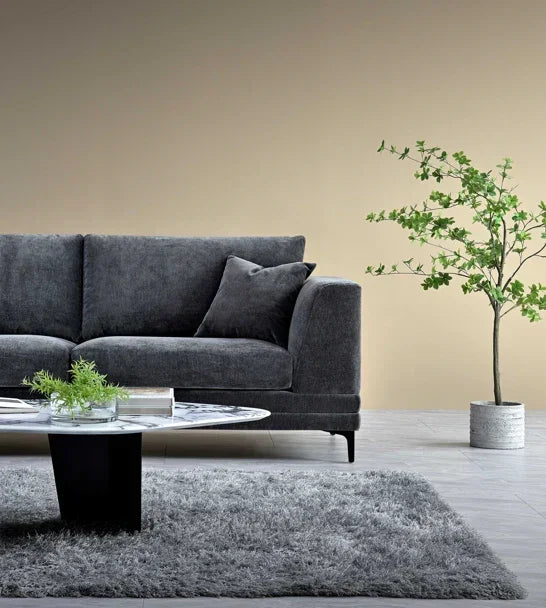 Charcoal fabric sofa with matching cushion beside round marble coffee table on grey rug