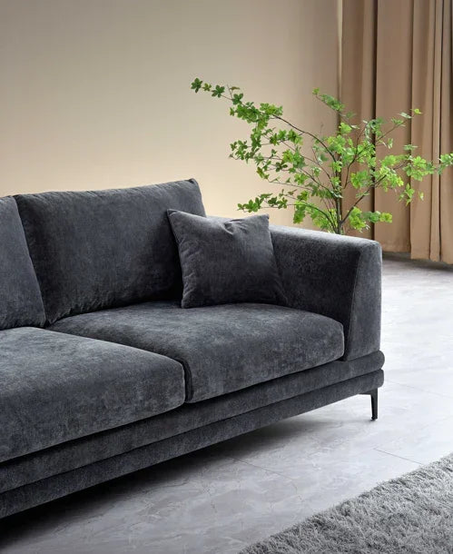 Dark grey fabric sofa with plush cushions beside green plant and neutral curtains