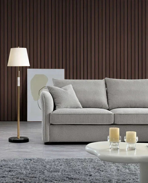 Light grey fabric sofa with cushions, gold floor lamp, and white coffee table in modern lounge