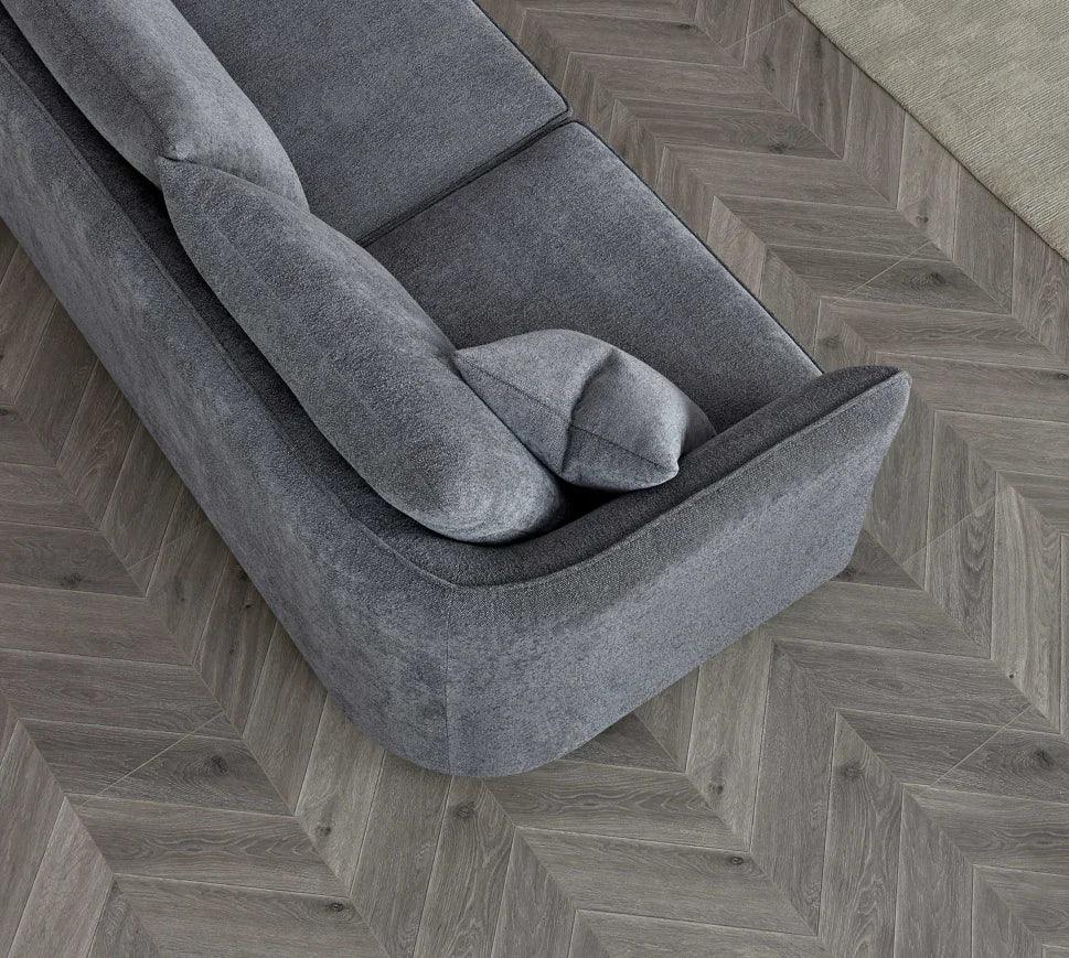 Grey fabric sofa with plush back cushions on herringbone wood floor