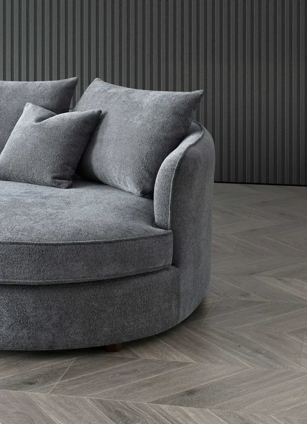 Grey round sofa with textured fabric and matching cushions on herringbone wood floor