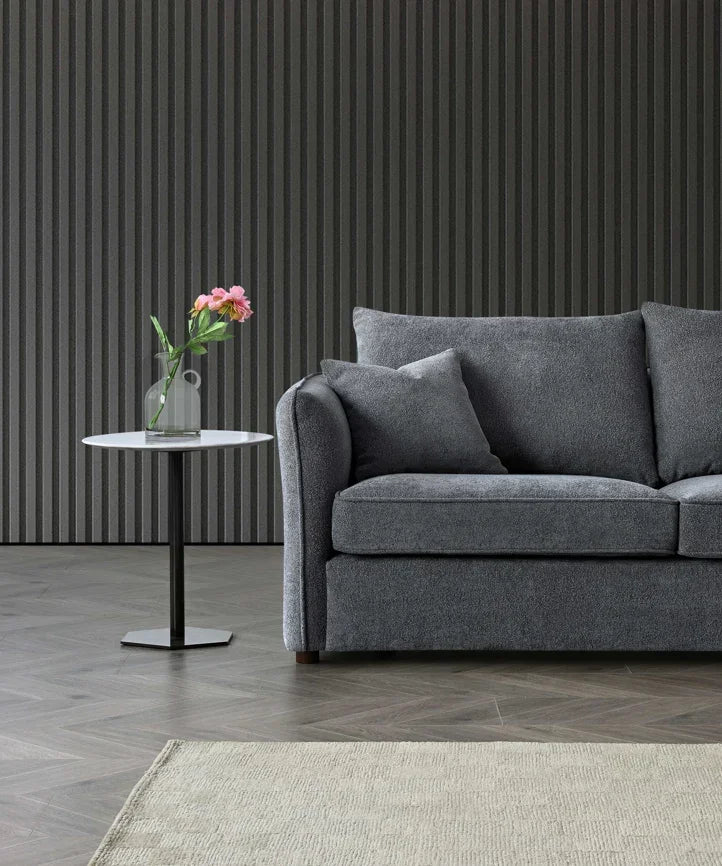 Grey fabric sofa with matching cushion beside round white side table and vase of flowers