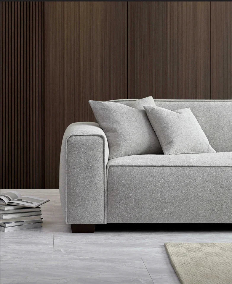 Light grey fabric sofa with two cushions, wooden legs, and books on a modern living room floor