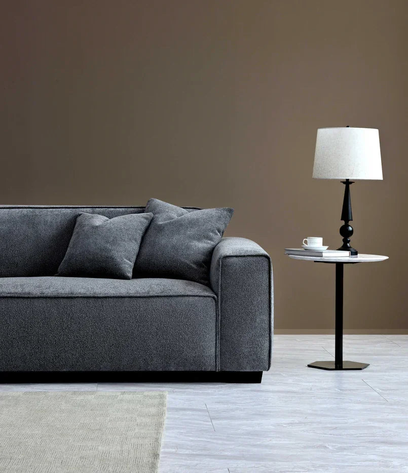 Grey fabric sofa with matching cushions beside a black side table and modern lamp