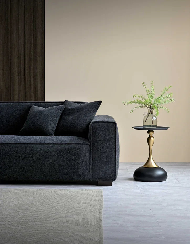 Dark fabric sofa with scatter cushions beside round gold side table and vase with greenery