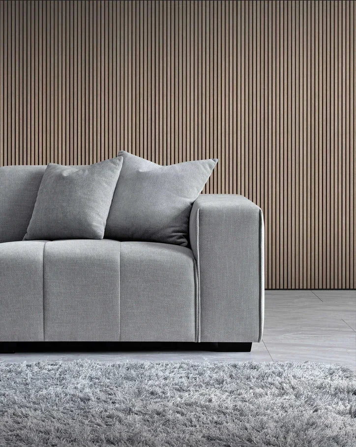 Light grey fabric sofa with matching cushions beside shaggy rug and wood panel wall