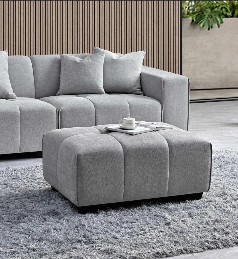 Grey fabric sofa with matching ottoman and cushions on a textured rug in modern living room