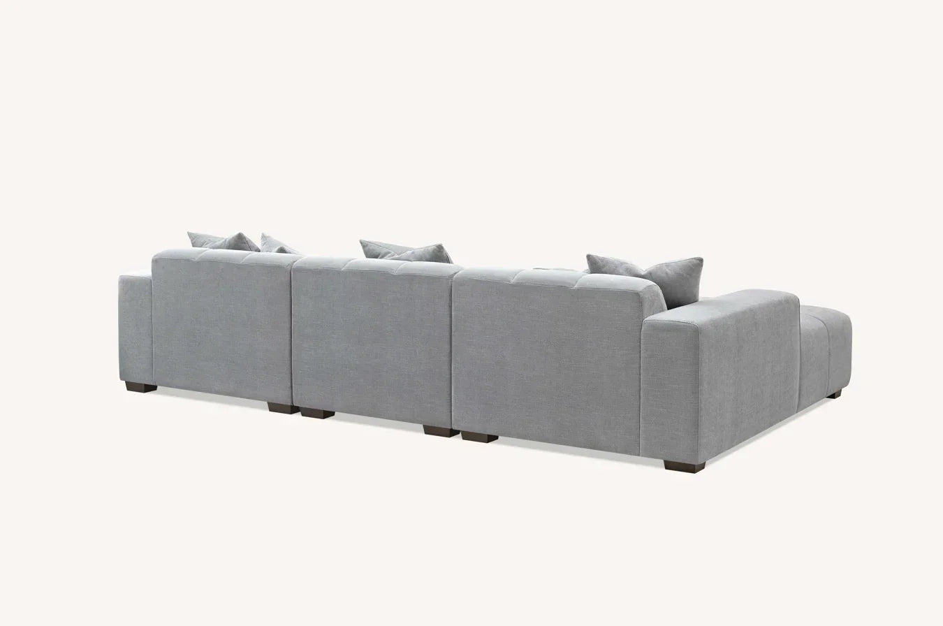 Back view of large light grey fabric corner sofa with cushions on light background