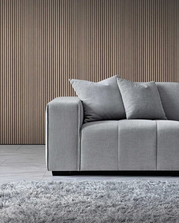 Grey fabric sofa with two cushions beside vertical wood slat wall and soft rug