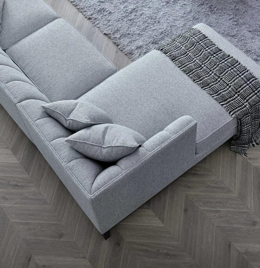 Grey corner sofa with chaise, textured throw and scatter cushions on herringbone floor