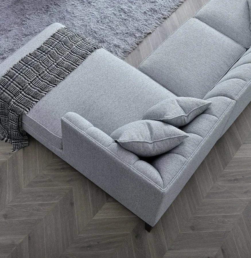 Grey fabric corner sofa with cushions and textured throw on herringbone wood floor