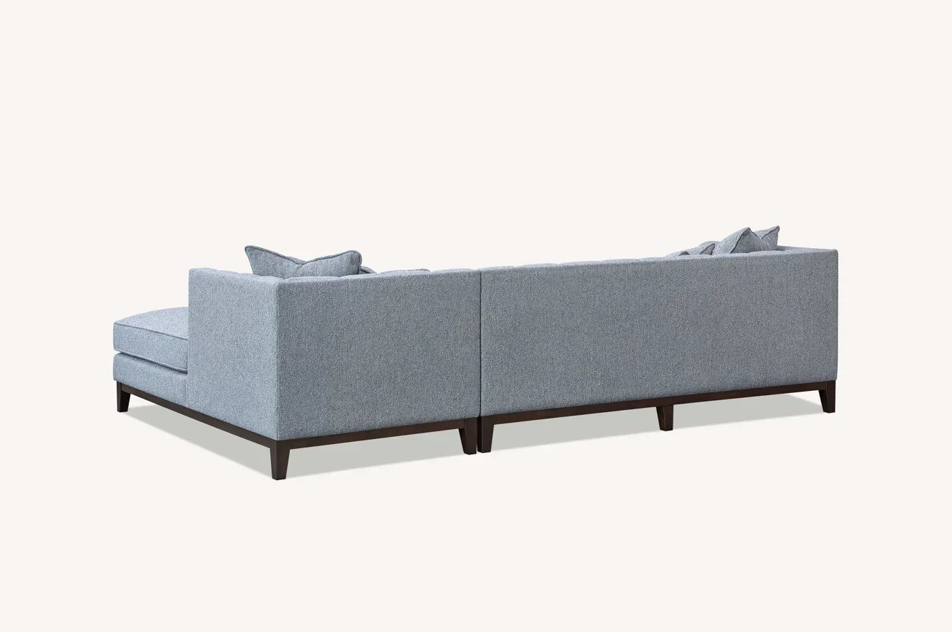 Rear view of modern grey fabric corner sofa with dark wood legs and scatter cushions