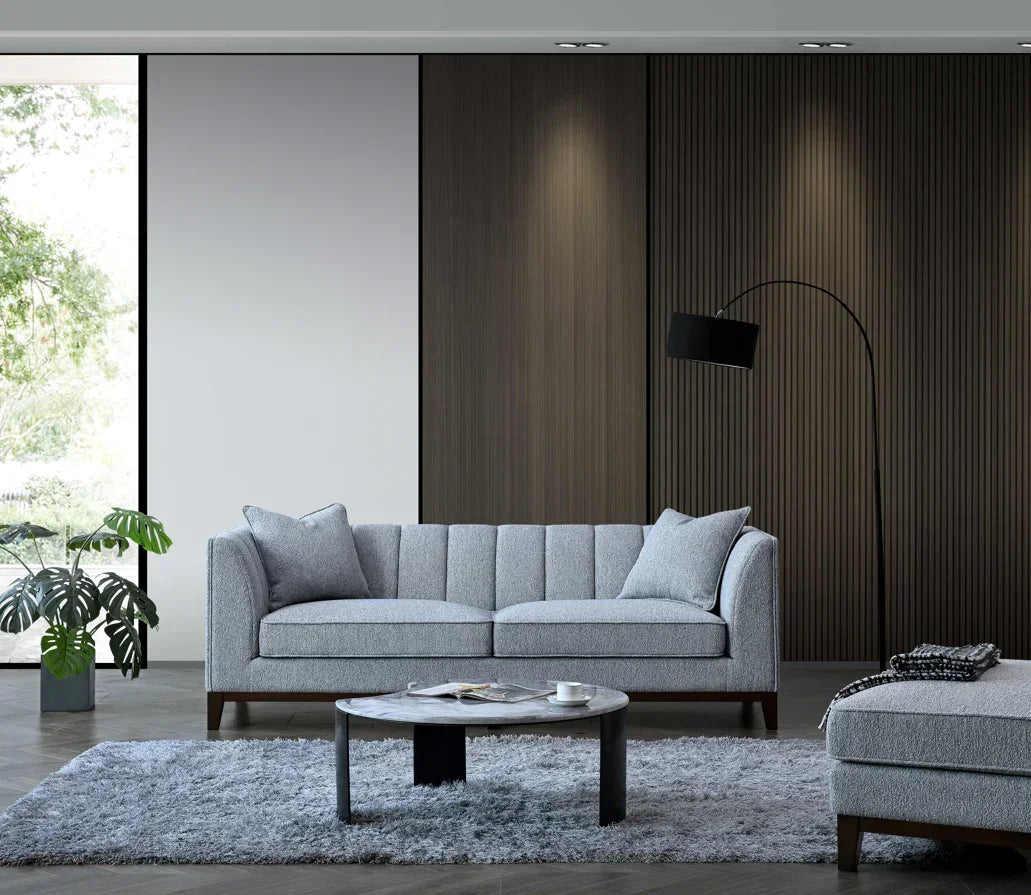 Grey fabric sofa with fluted backrest, matching ottoman and round coffee table in modern living room