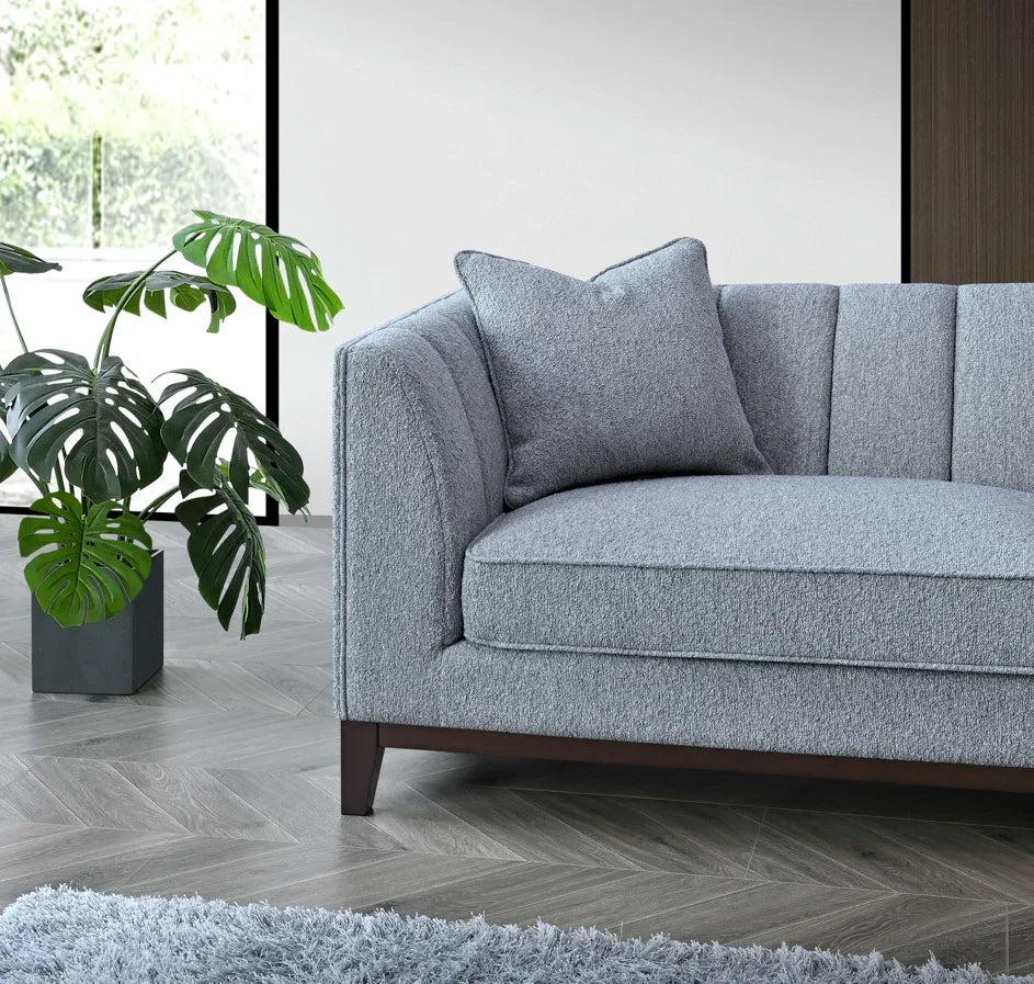 Grey fabric sofa with channel tufting and cushion near potted plant on chevron floor