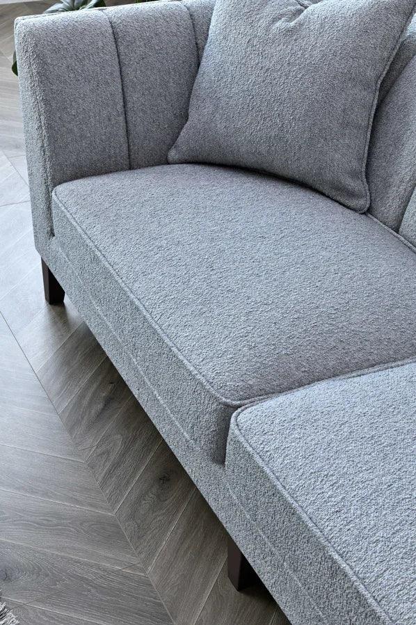Light grey fabric sofa with cushion and channel tufted backrest on wood floor