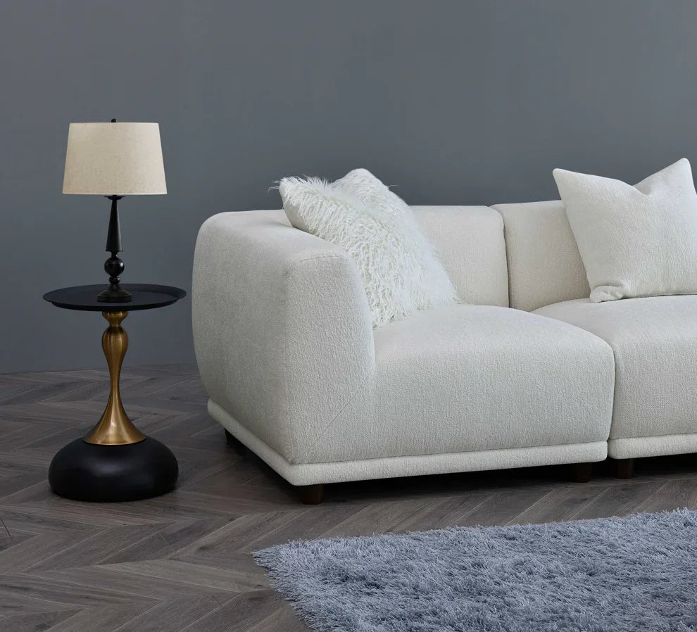 Ivory fabric corner sofa with textured cushions beside black and gold side table and lamp