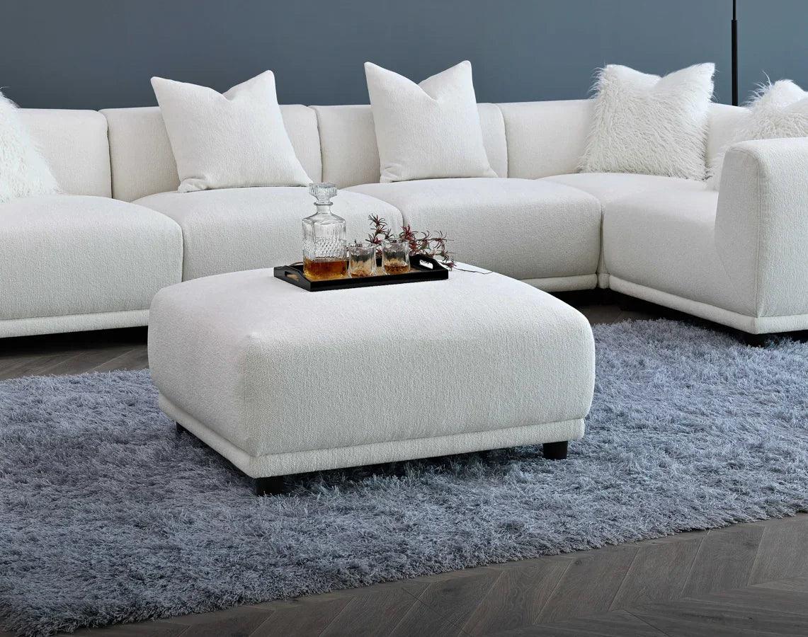 White corner sofa with matching ottoman and fluffy pillows on grey shaggy rug