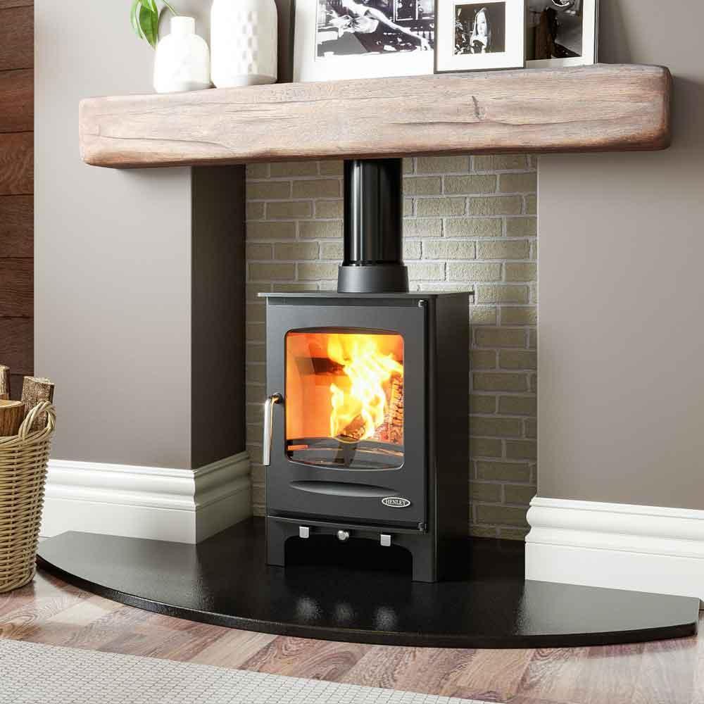 Modern wood burning stove with glass door set against light brick fireplace and wooden mantel