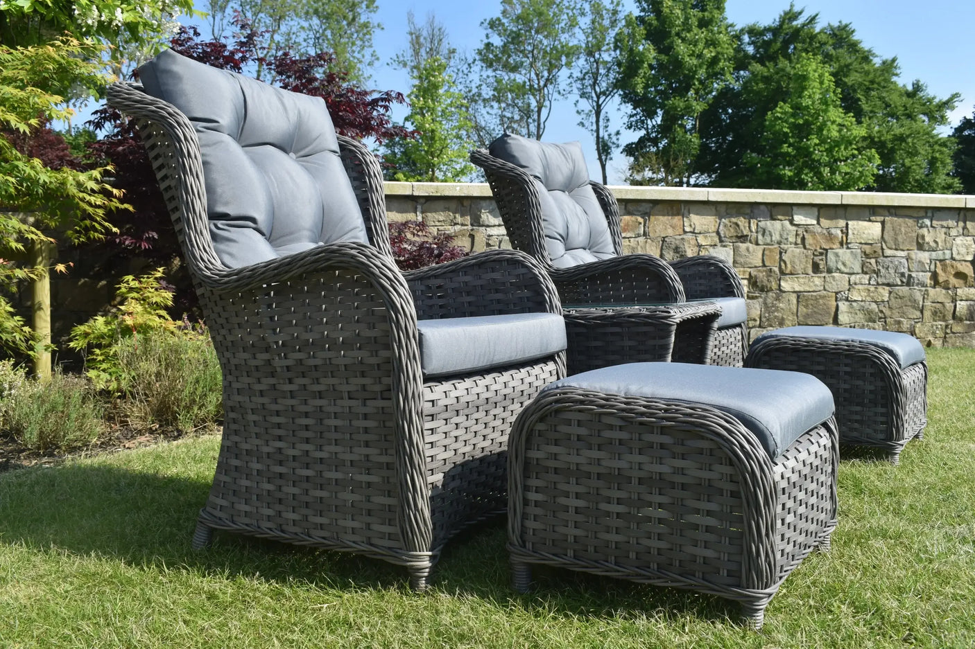 Grey rattan garden bistro set with cushioned chairs and ottomans on grass
