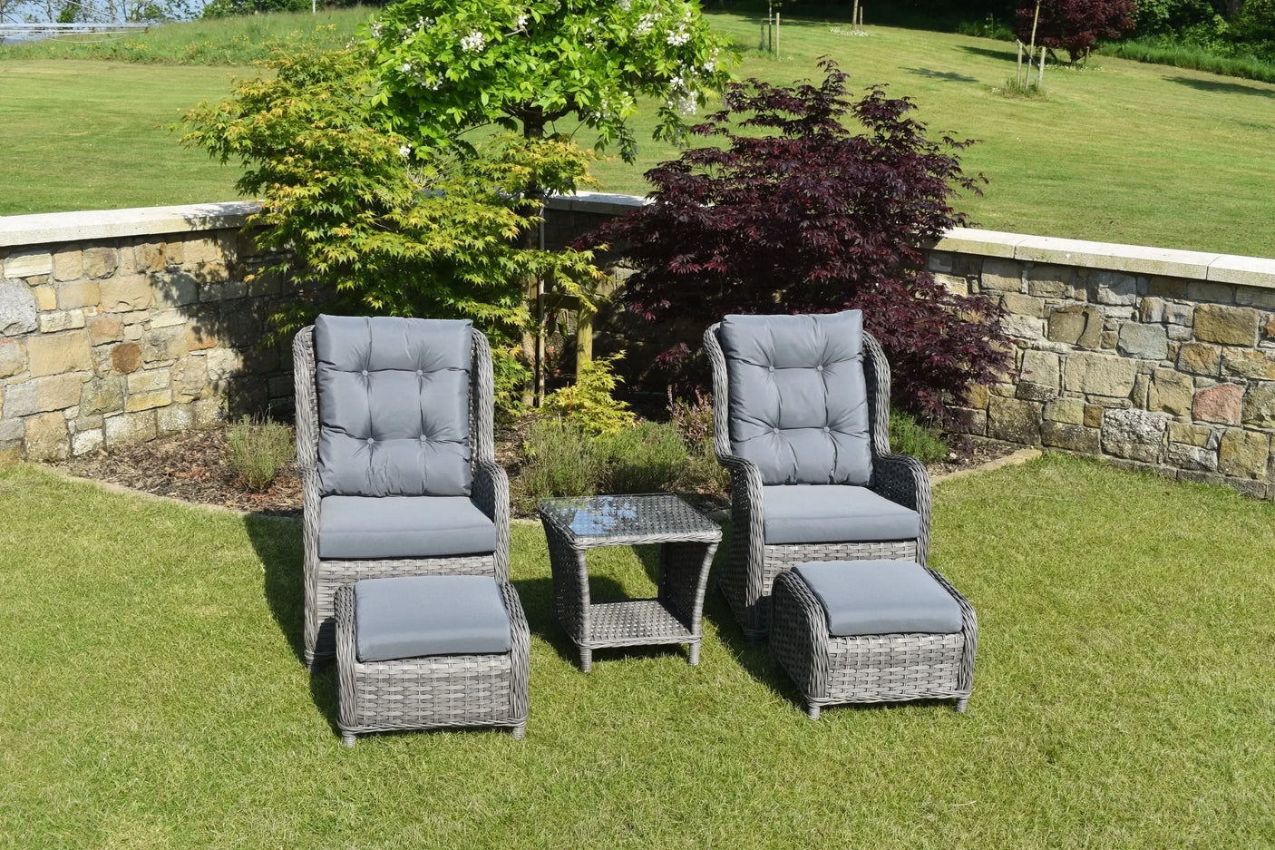 Grey rattan bistro garden set with two cushioned chairs, ottomans, and glass-top table on lawn