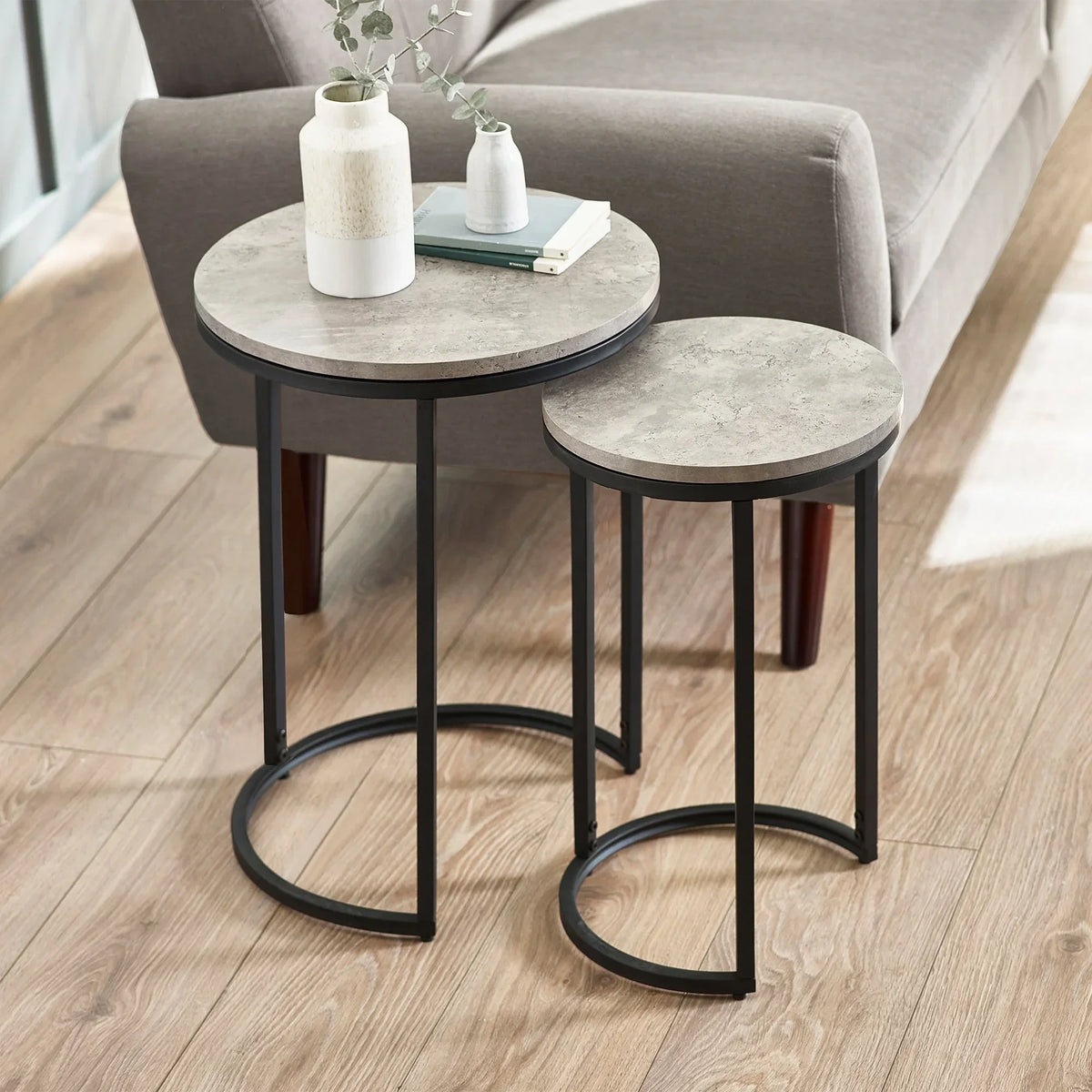 Round nesting side tables with stone-effect tops and black metal frames beside grey sofa