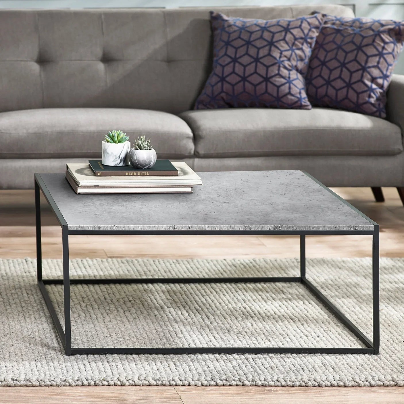 Square concrete effect coffee table with metal frame on textured rug in modern living room