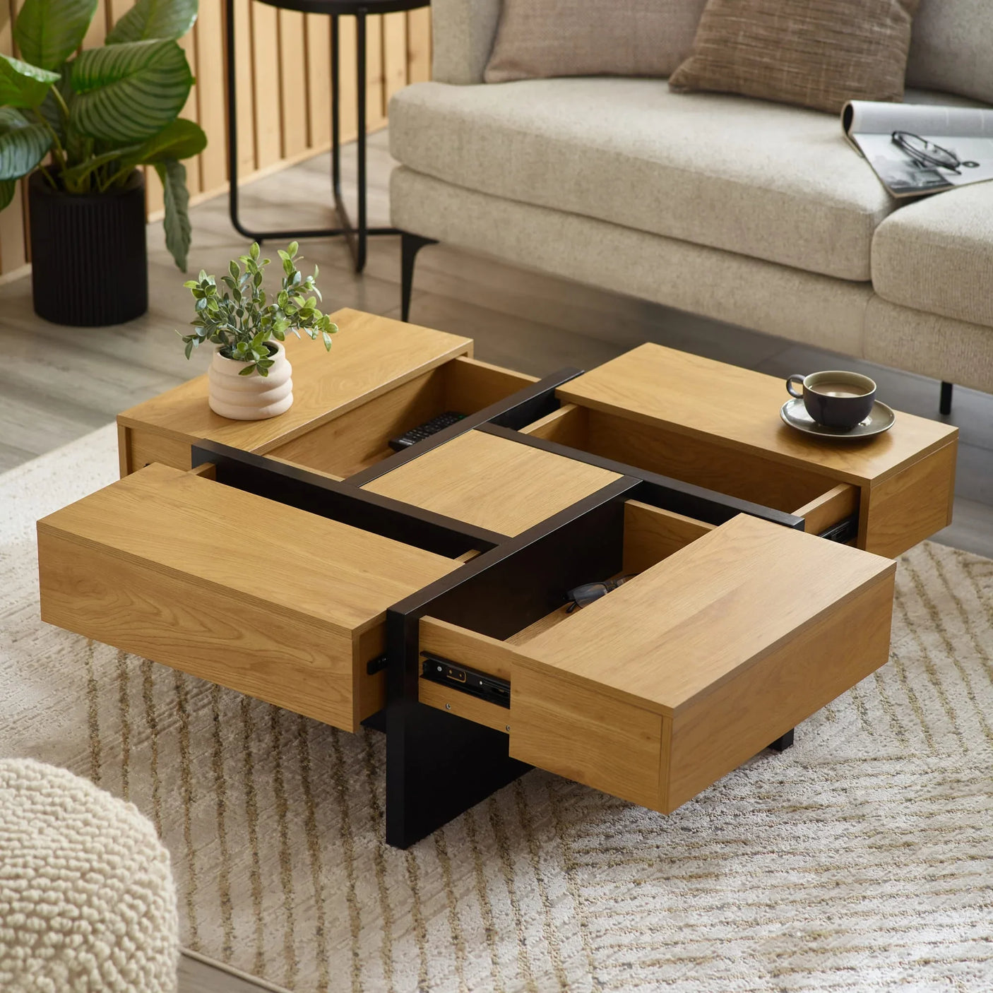 Oak coffee table with black frame, open storage drawers, cup and plant in modern living room