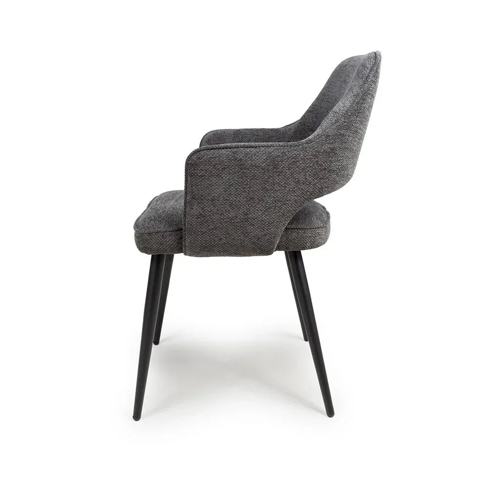 Grey upholstered dining chair with armrests and black metal legs, side profile view