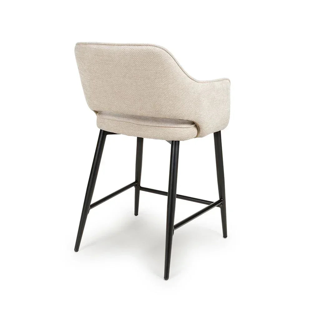 Beige fabric bar stool with curved backrest and black metal legs, rear angle view