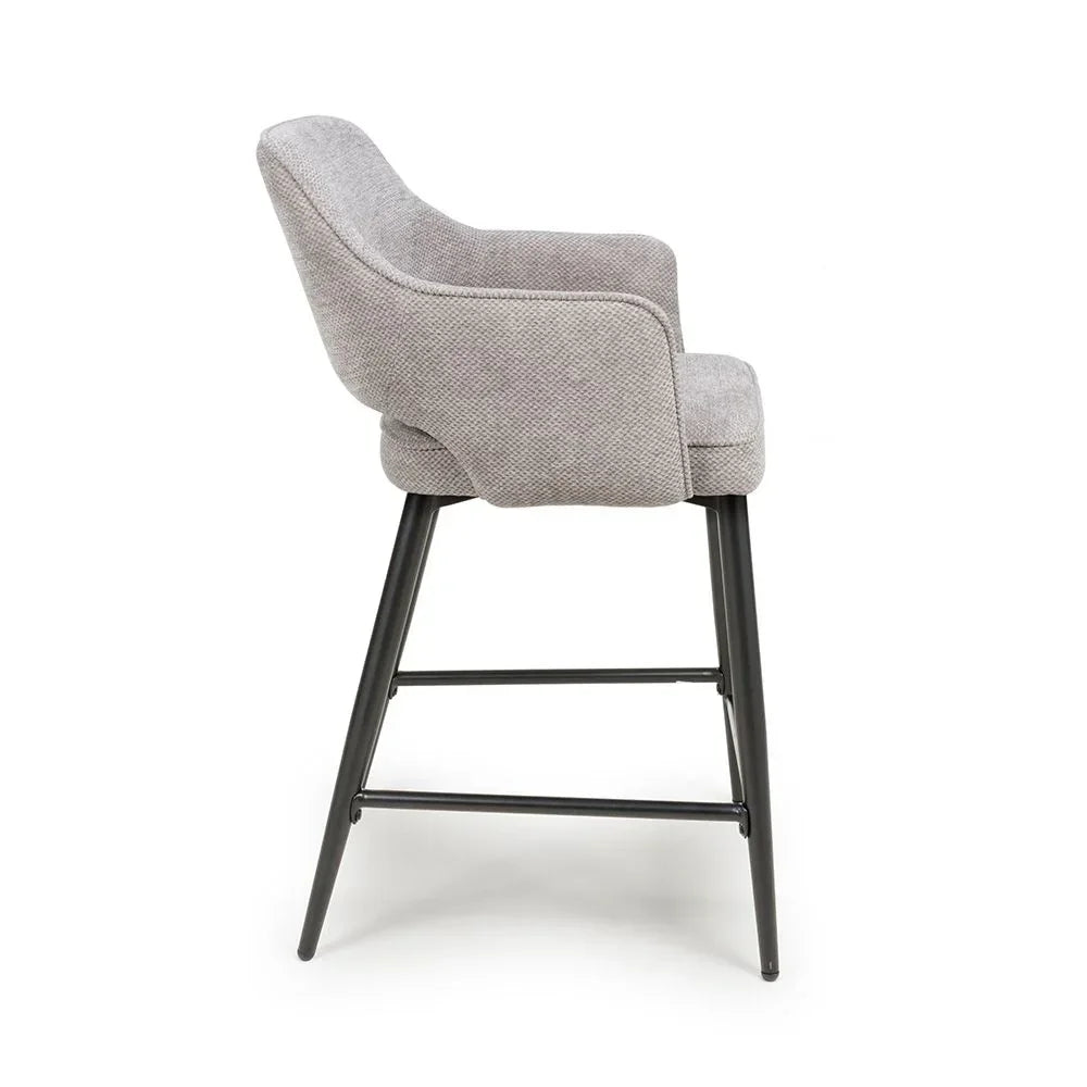Grey fabric bar stool with curved backrest and black metal legs, side profile view