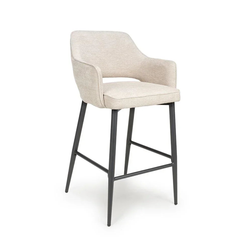 Beige upholstered bar stool with armrests and black metal legs on white background