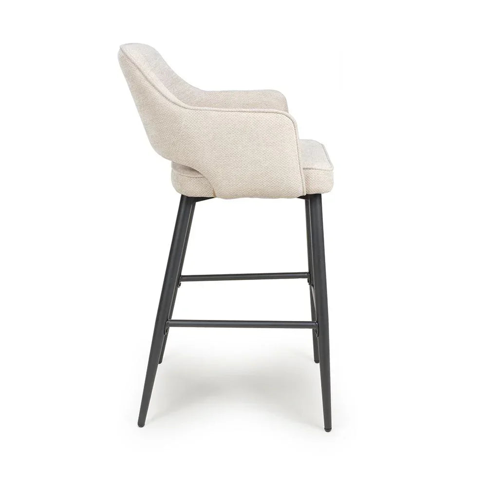 Beige upholstered bar stool with black metal legs shown from side view