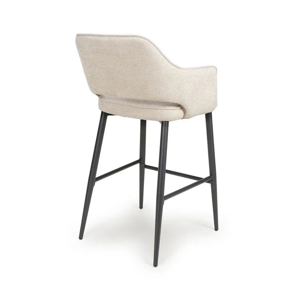 Beige upholstered bar stool with black metal legs shown from rear angle