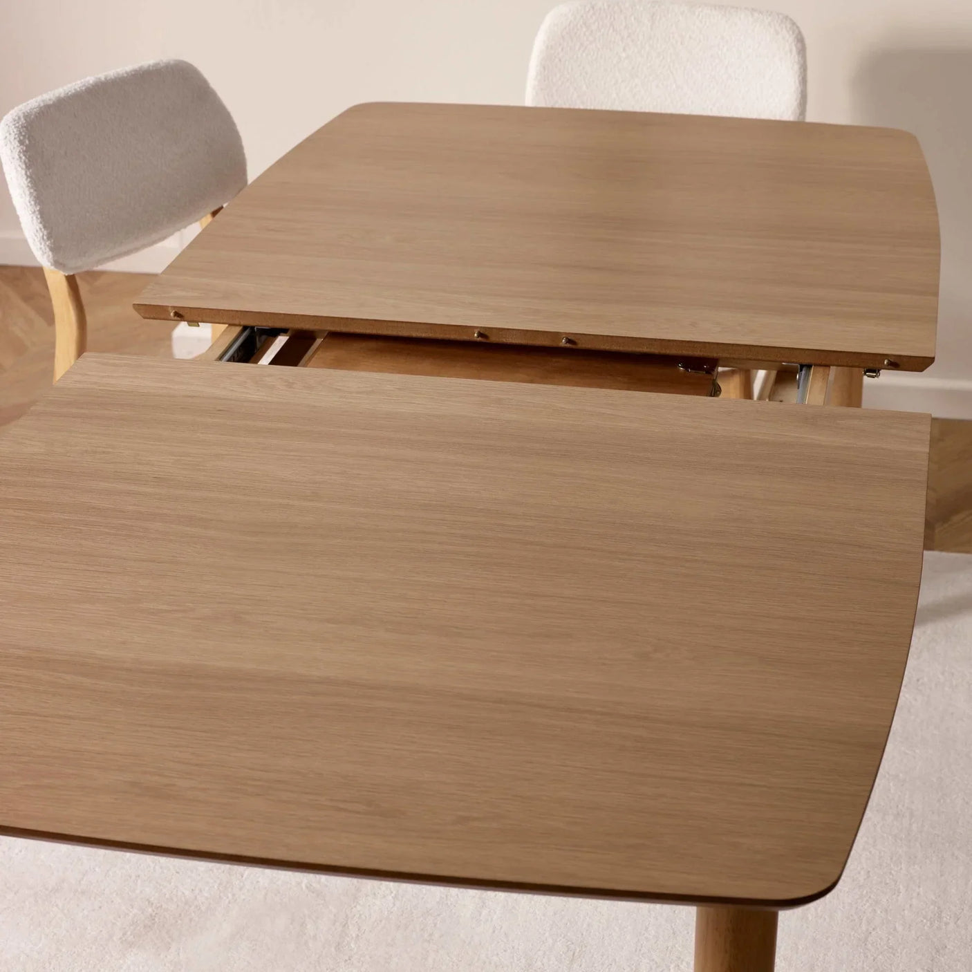 Oak extendable dining table with visible extension mechanism and two cream upholstered chairs