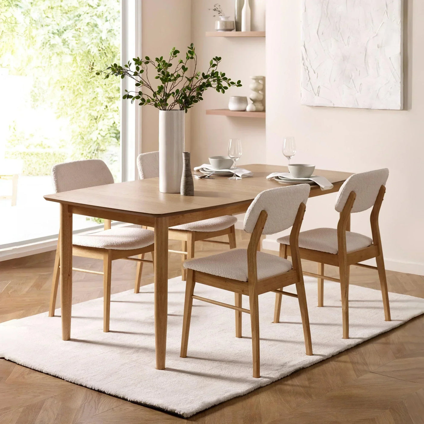 Light wood dining table set with four upholstered chairs on white rug in bright dining room